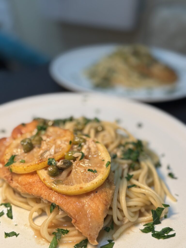 Plate of spaghetti with lemon-slice-topped chicken, herbs, and light sauce (close-up).
