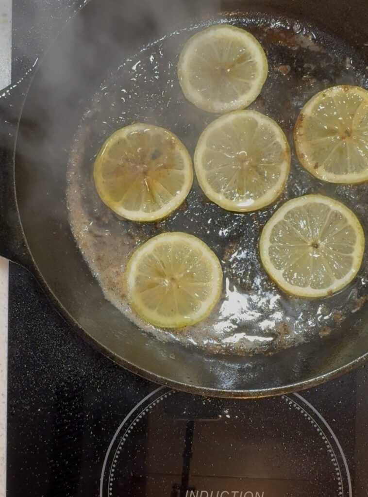 Lemon slices sizzling in a hot skillet with steam rising from the pan.